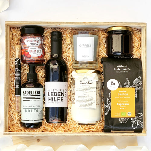 Hier siehst du eine holz Box.Diese Geschenkbox enthält: Vollkornige Brot-Backmischung, nachhaltige Vanille Duftkerze aus Recycling-Wachs, erfrischende Handseife, Fruchtaufstrich, Bio Salz mit einer angenehmen Rauchnote, leckere Tomaten-Salsa und Bio-Espresso sowie ein St. Laurent Rotwein 